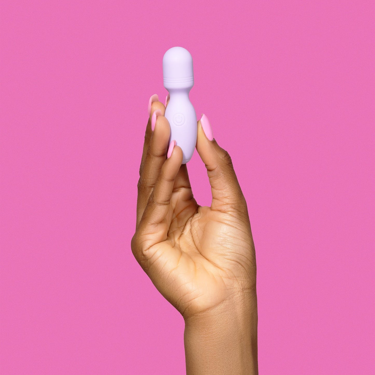 Hand holding a small light purple vibrator against a pink background