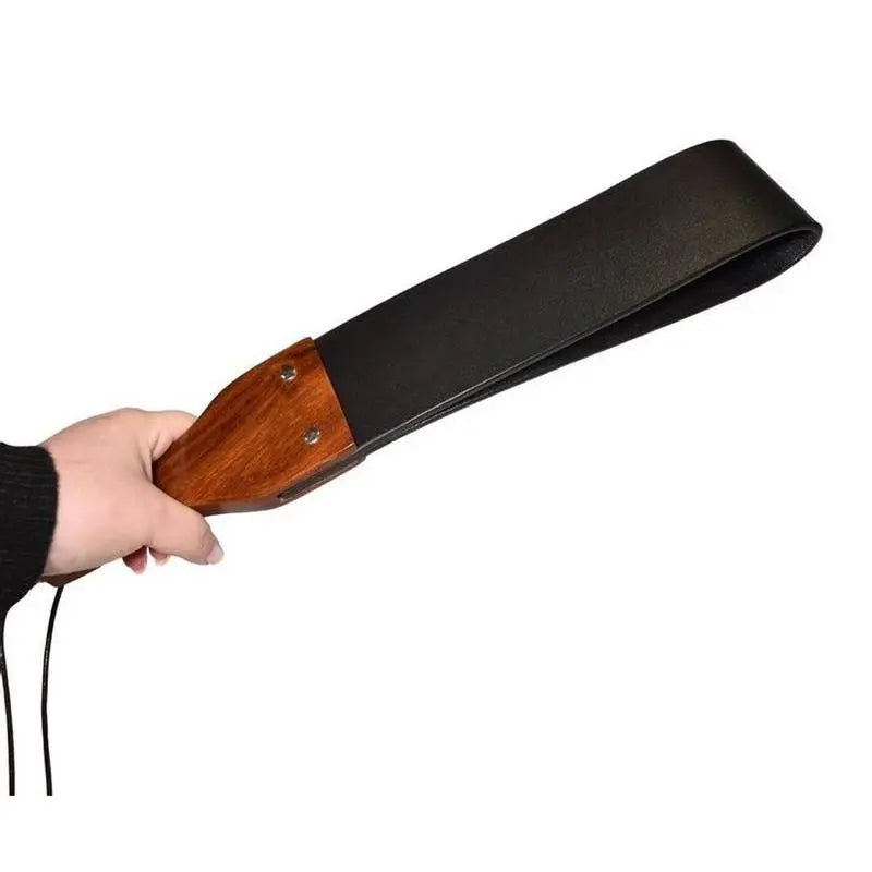 Leather and wood spanking paddle held in hand